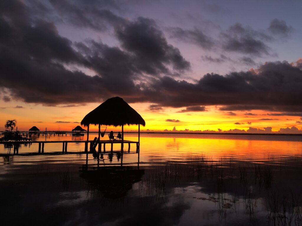 brown wooden beach house on body of water during sunset Bacalar